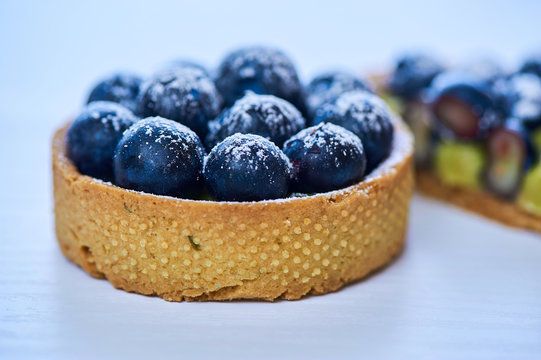 Hand made tarlets dessert from pistachio and chocolaty bakery dough with blueberry decoration on white background
