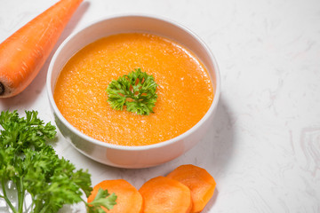 Carrot soup with cream and parsley on white stone background. Top view. Copy space