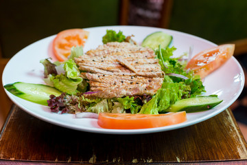 Steak with tomatoes, cucumbers and herbs on a white plate
