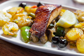 Baked salmon meat with potatoes and vegetables on a white plate in a restaurant