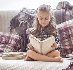 little girl reading book on sofa