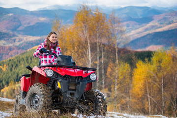Brunette girl in winter clothes rides a quad bike on a snowy road with stunning autumn views of...
