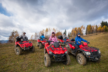 Young people in winter clothes on red atv off-road vehicles on a countryside trail in nature under...