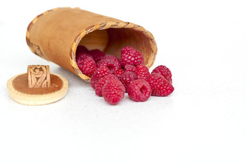 Raspberries near bark basket on a white background from the top 1