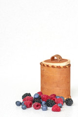 Blueberries, raspberries and blackberries near bark basket on a white background