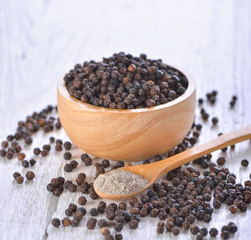 Black peppercorns powder on white wooden