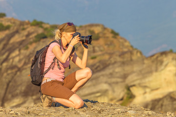 Nature woman photographer with camera takes picture outdoor. Caucasian female with backpack shooting on mountain top.Professional photographer takes photo of mountain landscape after hiking.Copy space