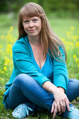 Naklejka na ściany i meble Caucasian woman with long hair, in a blue sweater and in jeans sits on the grass