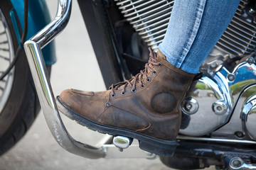 Close up, side view at female foot with protective brown boot on the stands of chopper motorbike with protective arcs
