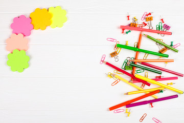 Colorful pencils and felt-tip pens, color notepaper, paper clips, stationery nails on white wooden background