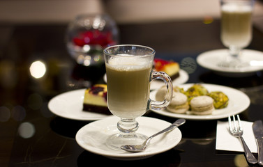 Hot latte in a glass whith macarons behind