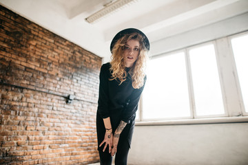 Beautiful curly girl in a bonnet standing against a brick wall and glances at the camera