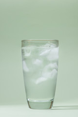Ice drinking water glass on table over green.
