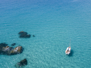 Vista aerea di una barca ormeggiata che galleggia su un mare trasparente. Immersioni relax e vacanze estive. Coste italiane, spiagge e rocce