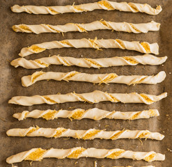 Homemade Raw Breadsticks before baking. Twisted strips of raw dough with cheese and sesame seeds freshly prepared for baking.