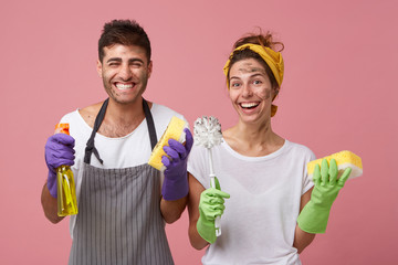 European male wearing apron and female in white T-shirt smiling broadly being glad to clean...