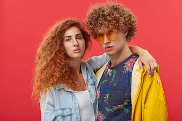 People, relationships, style, fashion and modern lifestyle. Studio portrait of two male and female best friends with ginger hair standing close to each other, girl with freckles hugging man in shades