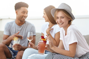 Group of happy young people toasting to love and prosperity, having alcohol drinks at rooftop party. Three cheerful friends enjoying nice time together, having fun at terrace cafe, drinking cocktails