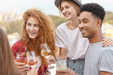Students having university-leaving party clinking their glasses with wine and cocktails being happy to graduate. Friendly company of youngsters gathering together embracing and toasting with drinks