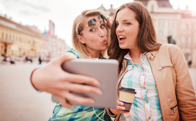 Young smiling girls enjoying in the city, have fun with tablet. Lifestyle, technology