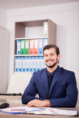 Smiling happy entrepreneur in business suit at his work place. Image of succesful positive businessman at his new modern office