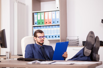 Fototapeta premium Businessman in office with his feet on the table looking in a blue folder. Image of realaxing corporate worker but still working. Working break