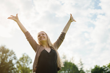 female teen girl standing in park with arms stretched to the sky