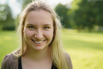 teen girl smiling in green park in sunny summer evening