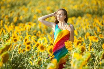Naklejka na ściany i meble On the yellow field of sunflowers stands a young woman, a summer bright day.