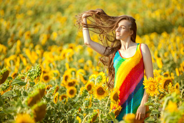 Woman with long hair is standing in the field among sunflowers.
