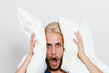 Angry man closing ears with pillows
