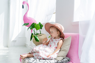 Fototapeta na wymiar Little girl sitting with lollipop on coach in living room at home with hat