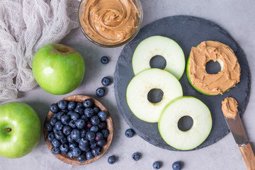 Green apple rounds with peanut butter and blueberries on slate board, horizontal, top view