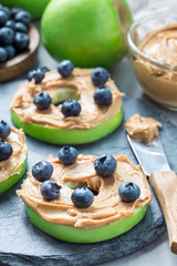 Green apple rounds with peanut butter and blueberries on slate board, vertical