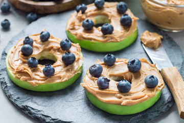 Green apple rounds with peanut butter and blueberries on slate board, horizontal