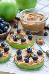 Green apple rounds with peanut butter and blueberries on wooden table, vertical