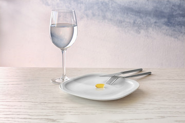 Plate with fish oil capsule, glass and flatware on light background
