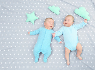 Beautiful baby twins lying together on bed sheet