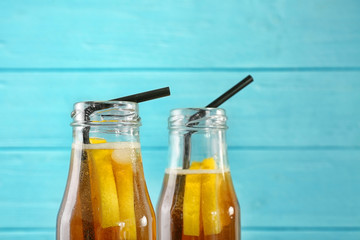 Bottles of fresh black tea lemonade on color background