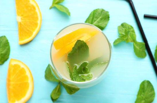 Glass of fresh orange lemonade on color background