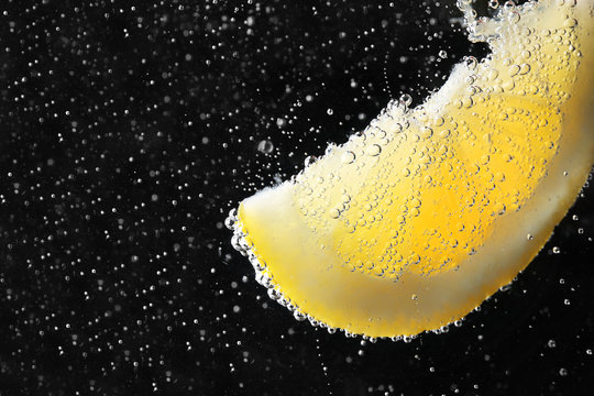Lemon slice under water with bubbles on black background, close up