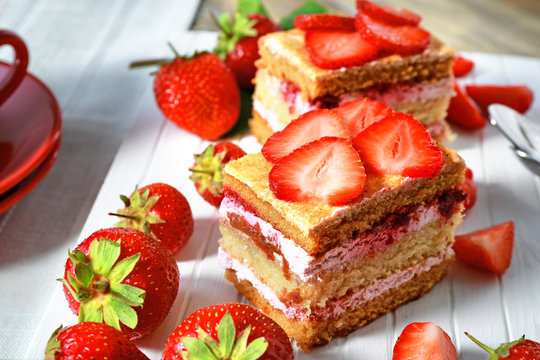 Two pieces of cake with strawberries on wooden board