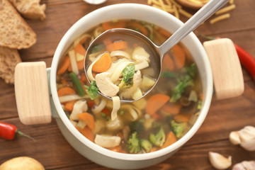 Ladle with turkey soup over saucepan on table