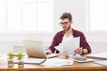 Young concentrated businessman using laptop in modern white office