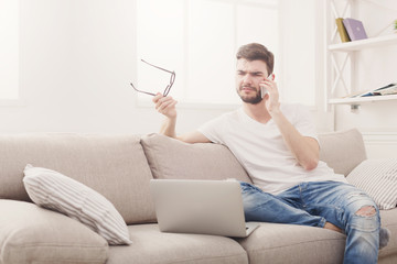 Serious young man at home with laptop and mobile