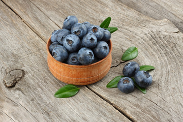 blueberries with green leaf in wooden bowl on old wooden table background