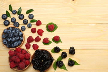 mix of blueberries, blackberries, raspberries in wooden bowl on light wooden table background. top view with copy space