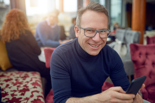 Attraktiver Mann mit Brille und seinem Smartphone blickt in die Kamera