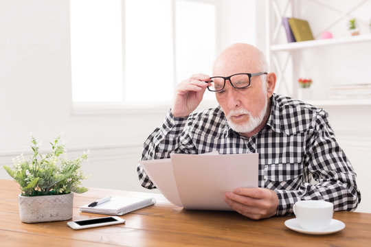 Shocked senior man looking at bills copy space
