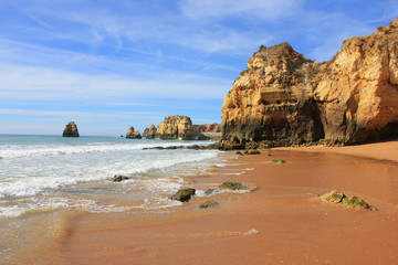 Fototapeta na wymiar Scenic hidden beach shore cliff rocks, sand waves, sunny summer day with no people. Algarve region in Portugal ocean water coast line outdoor landscape. Travel tourism vacation trip concept background